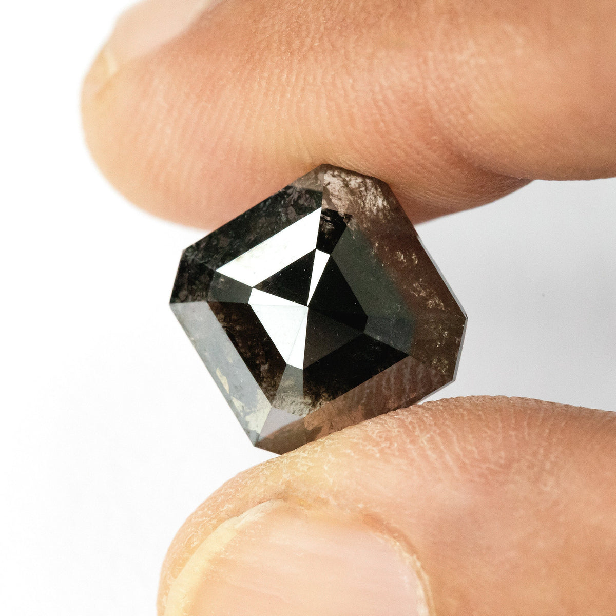 Brownish-black rose-cut diamond tilted between fingertips, showing a large white reflection and brown patches through the stone.