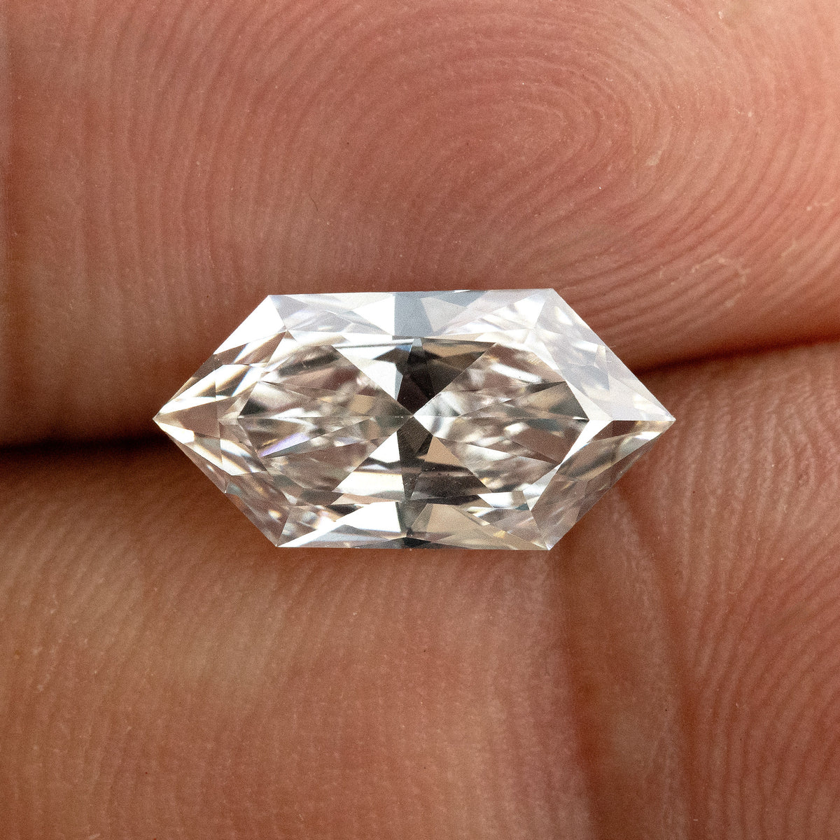 Horizontal macro shot of an elongated geometric hexagon diamond showing facet pattern against finger skin.