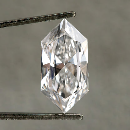 Studio face-up view of an elongated hexagonal diamond held vertically in tweezers on neutral gray background.