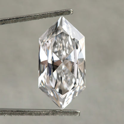 Colorless elongated hexagon cut diamond held in tweezers under crisp illumination against gray background.