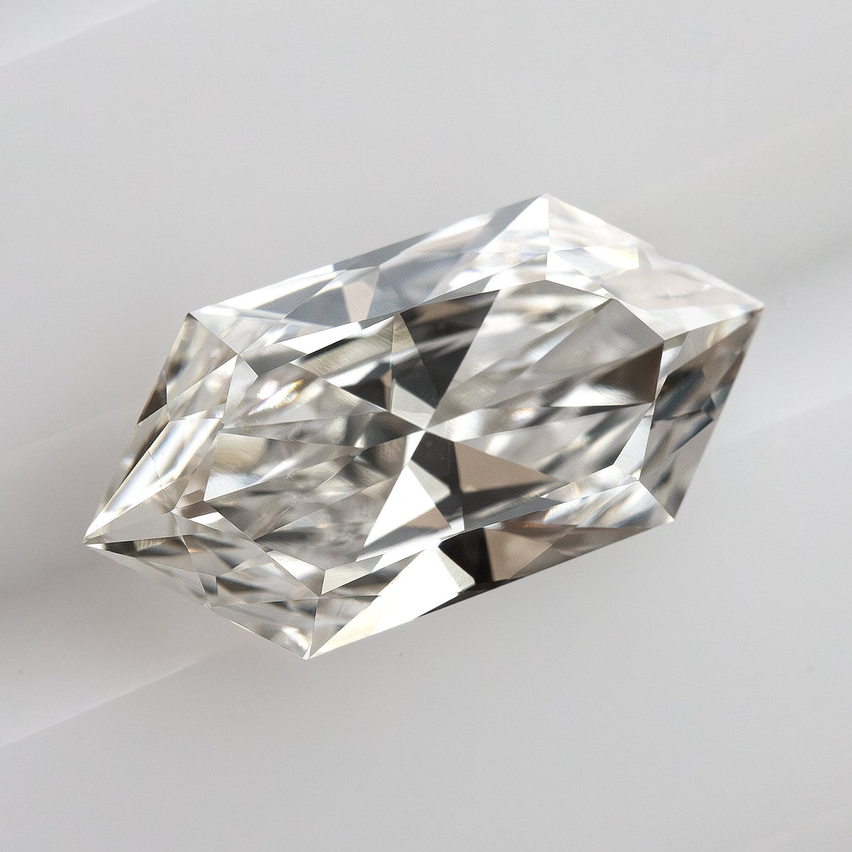 Oblique angle showing facet structure and depth of an elongated hexagon cut gemstone on a white grooved surface.