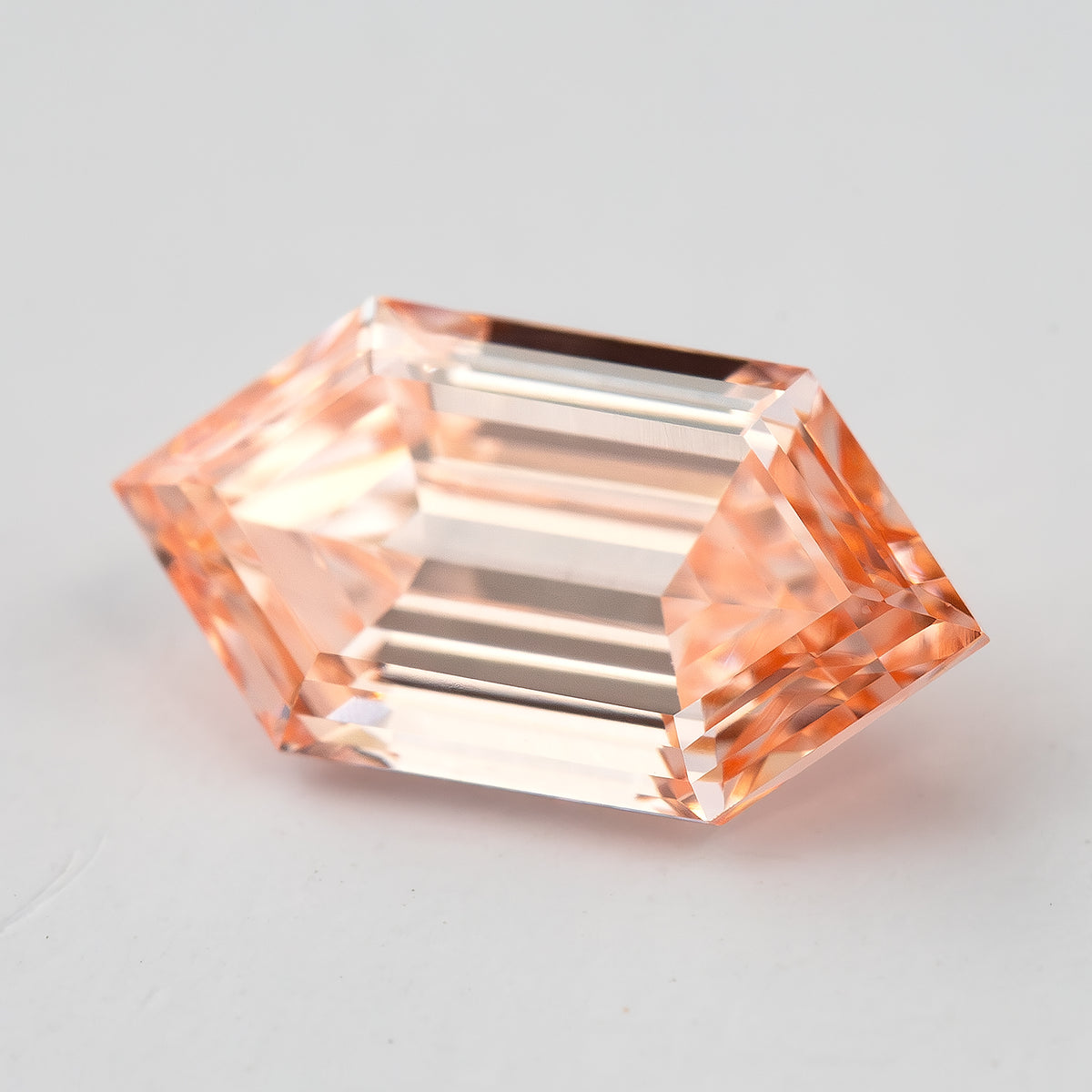 Bright angled view showing the diamond's transparent step pattern and peach pinkish orange appearance.