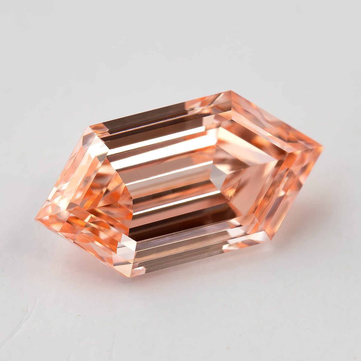 Angled face-up view of the loose diamond showing its elongated six-sided outline and warm peach tone.