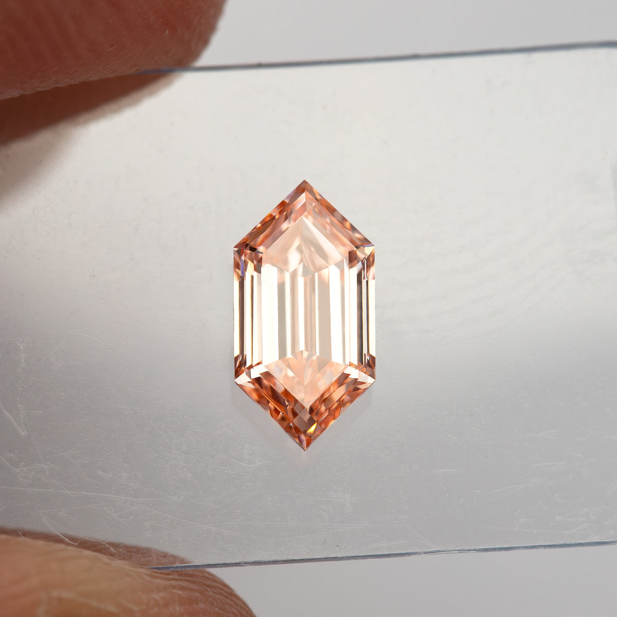 Small face-up view between fingers showing the scale of the 8.52 by 4.32 mm loose diamond.