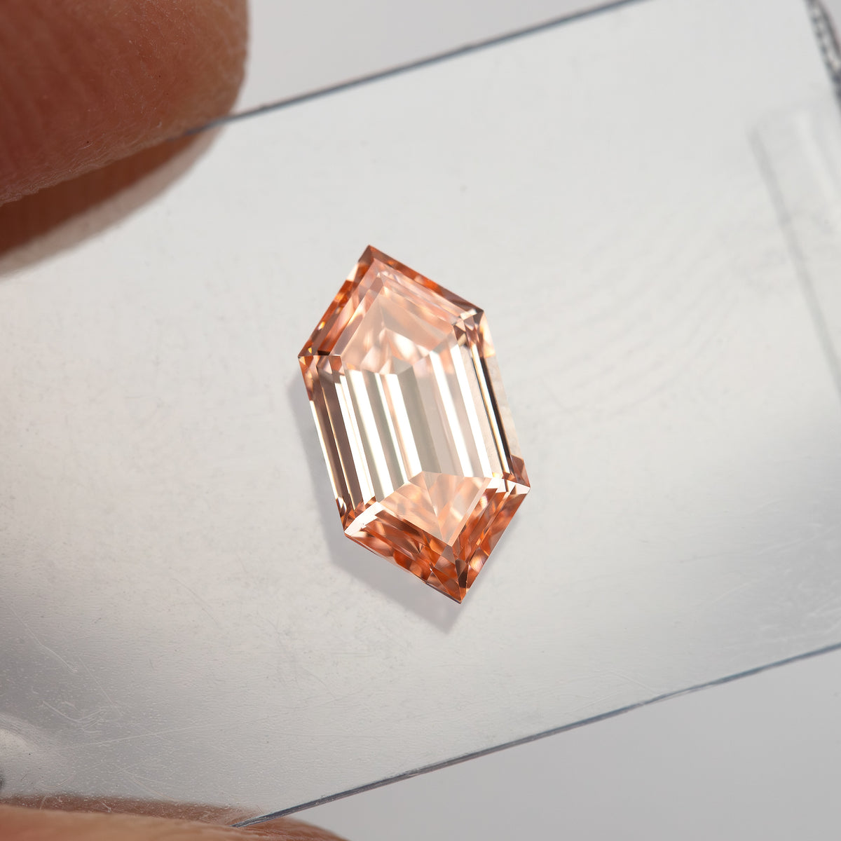 Angled scale view between fingers showing the diamond's slender proportions and peach tone.