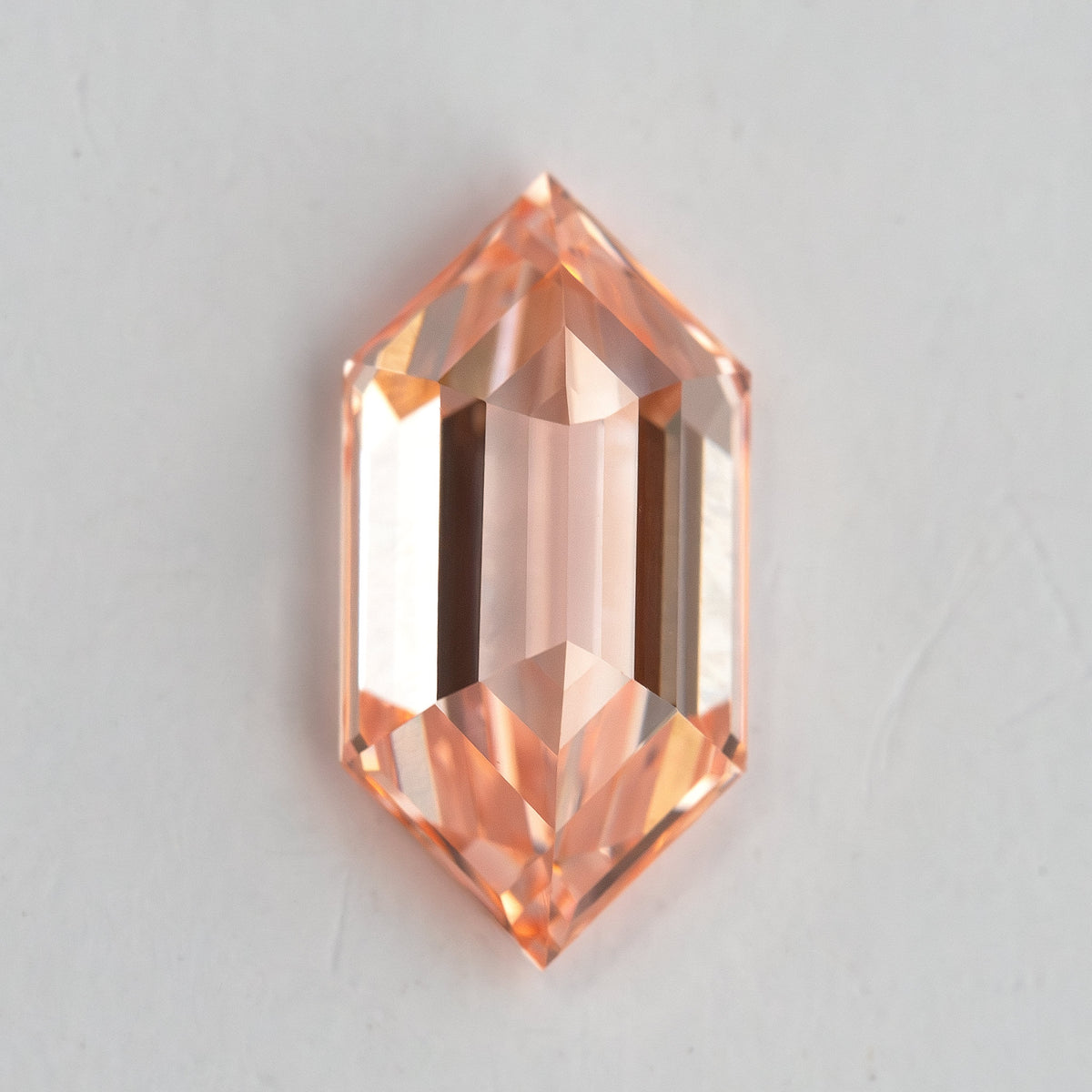 Pavilion-side view of the peach pinkish orange lab-grown diamond, showing its elongated keel and reverse facet geometry.