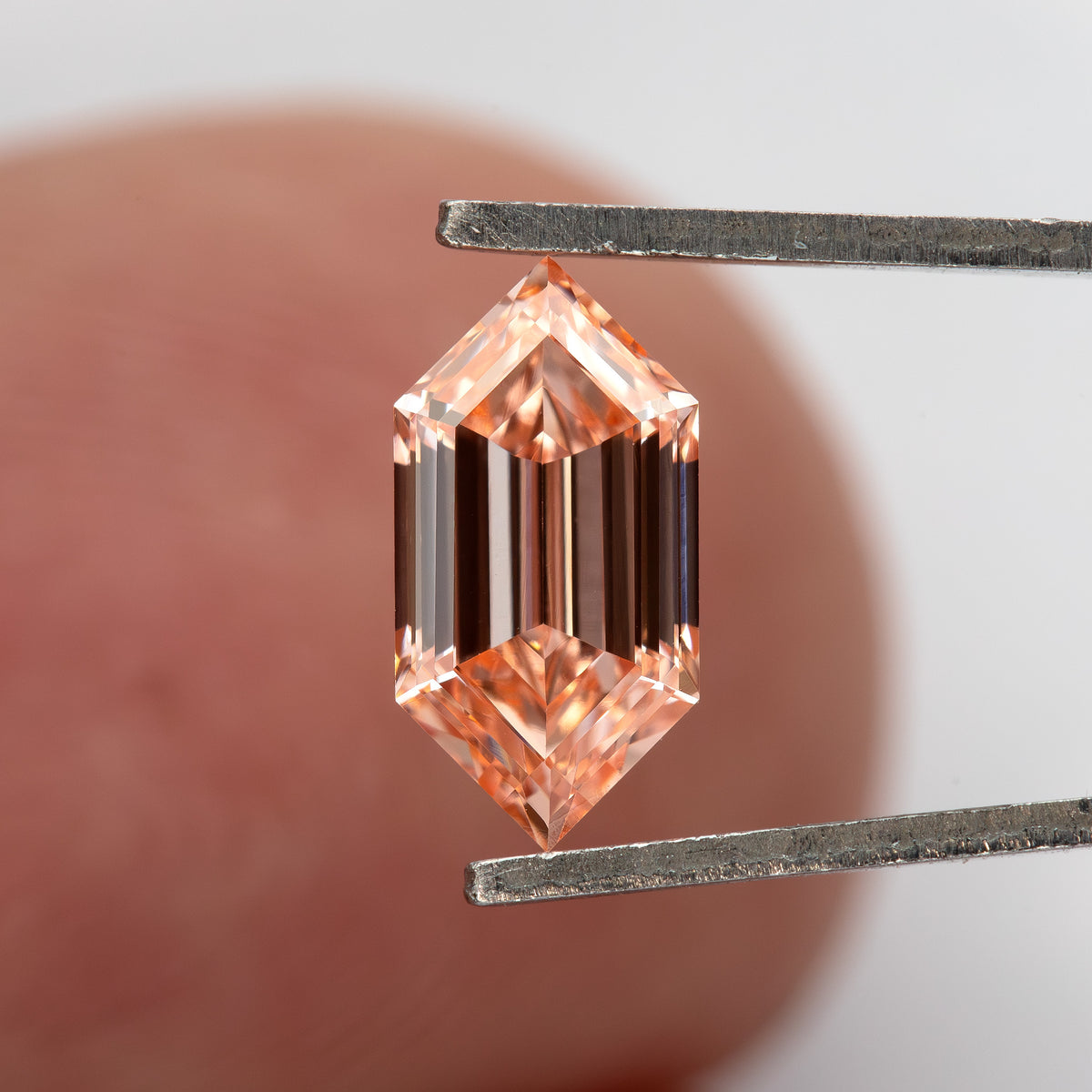 Diamond held in tweezers against a finger for scale, with dark and bright step reflections visible.