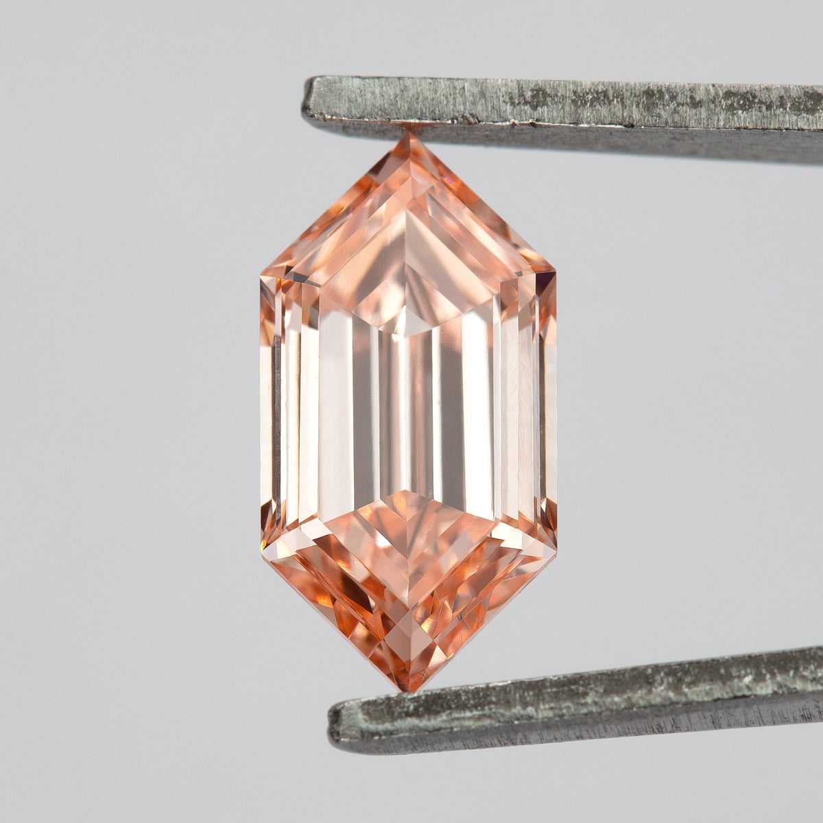 Vertical tweezer view under bright light showing pale peach color and elongated geometric faceting.