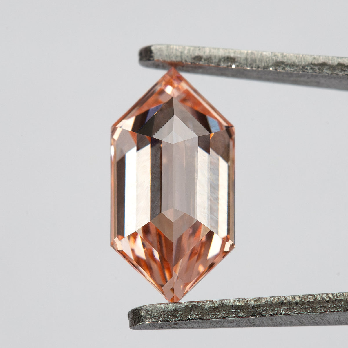 Angled tweezer view showing the step-cut pattern and deeper peach color near the pointed ends.