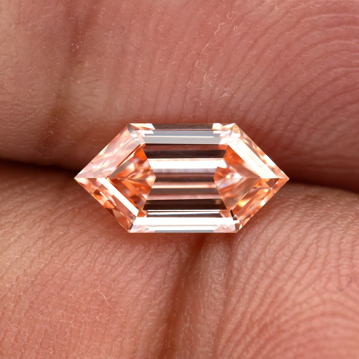 Horizontal finger view showing the exact diamond at hand scale with dark central step reflections.