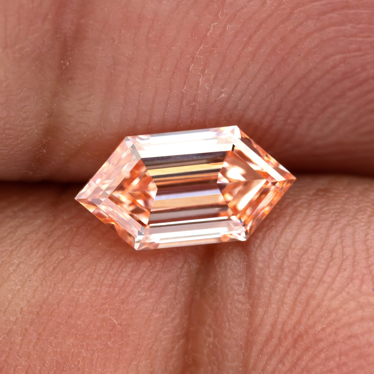 Horizontal finger view of the peach lab-grown diamond with bright edges and geometric center facets.