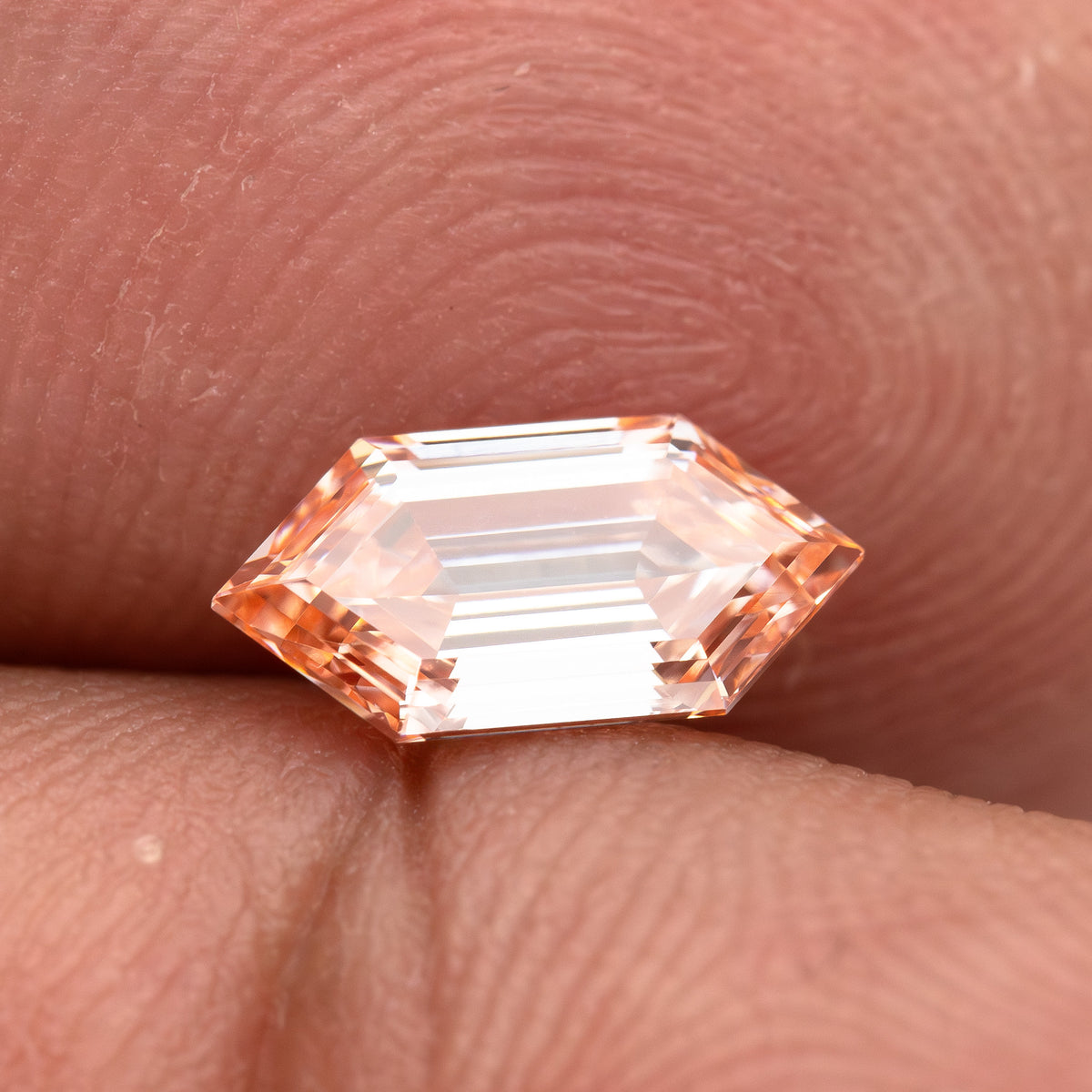 Side-angled finger view showing the diamond's low profile, pointed outline and peach color.