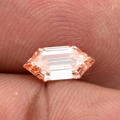 Side-angled finger view showing the diamond's low profile, pointed outline and peach color.