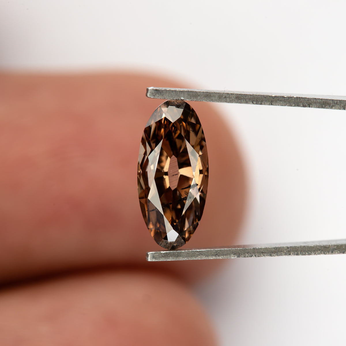 1.43 ct pinkish-brown lab-grown elongated oval diamond, finger scale in tweezers, SKU BLD154