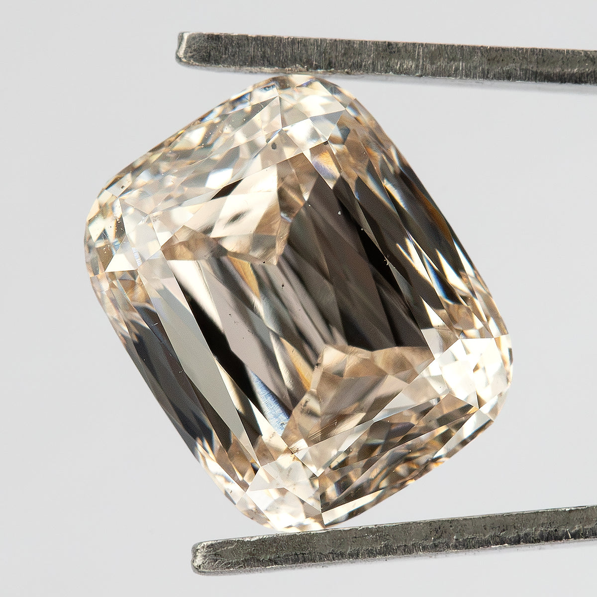 Three-quarter face-up view of the elongated cushion diamond held in tweezers, showing the crown facets and warm reflections.