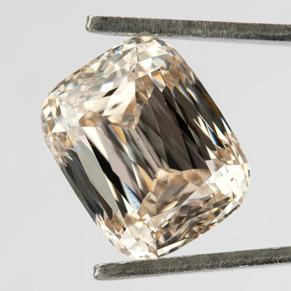 Three-quarter face-up view of the elongated cushion diamond held in tweezers, showing the crown facets and warm reflections.