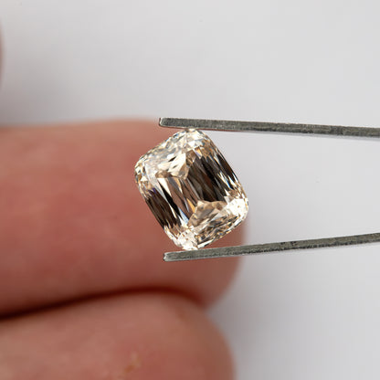 The diamond held in tweezers in front of a fingertip, providing scale while showing the full outline.