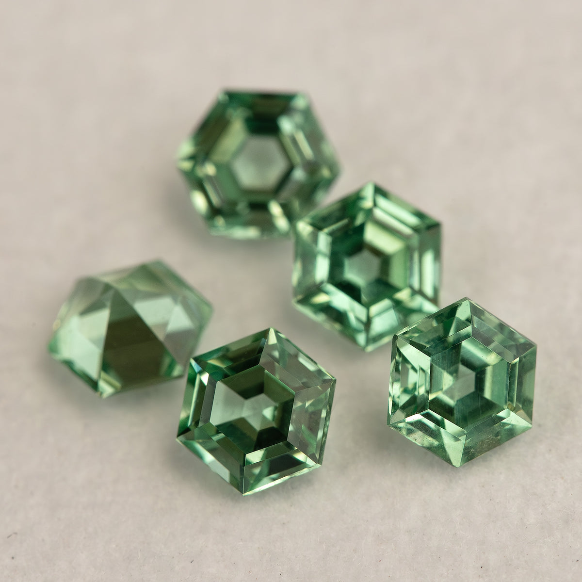 Mint green hexagonal lab-grown sapphires clustered on a pale base, showing tilted faces and green edge reflections.
