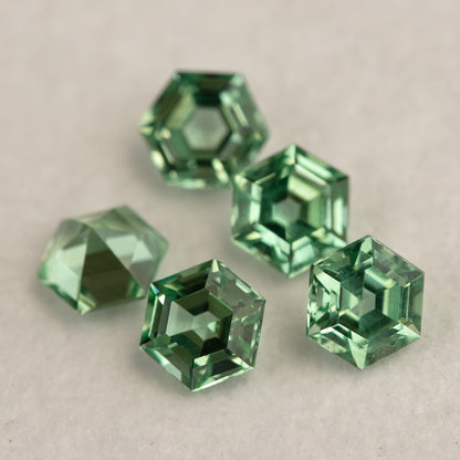 Mint green hexagonal lab-grown sapphires clustered on a pale base, showing tilted faces and green edge reflections.