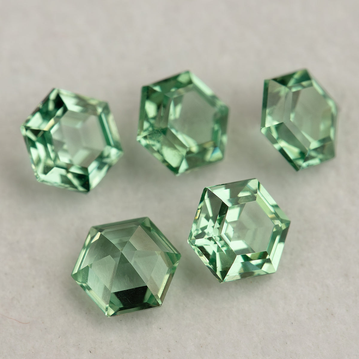 Five mint green hexagonal lab-grown sapphires spread on a neutral surface, showing varied light reflections.
