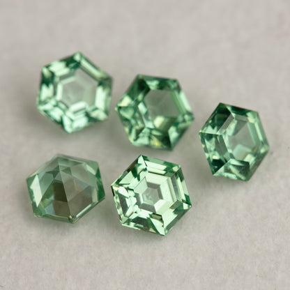 Mint green hexagonal lab-grown sapphires scattered on a pale surface with alternating bright and darker faces.
