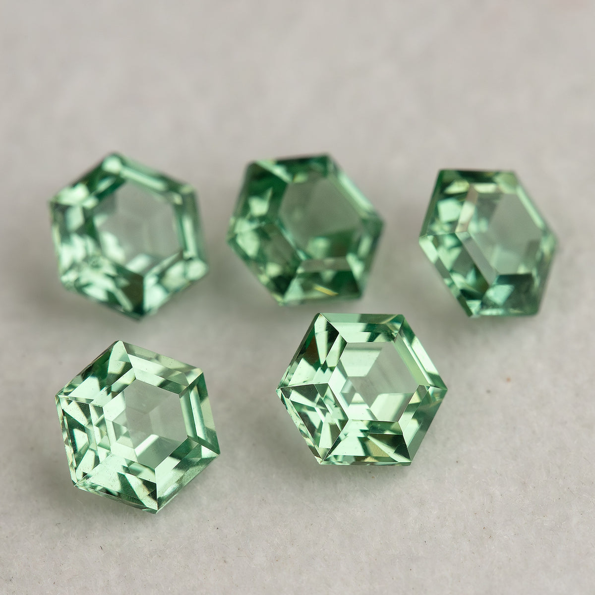 Five mint green hexagonal lab-grown sapphires on a neutral base, with pale reflections in their central faces.