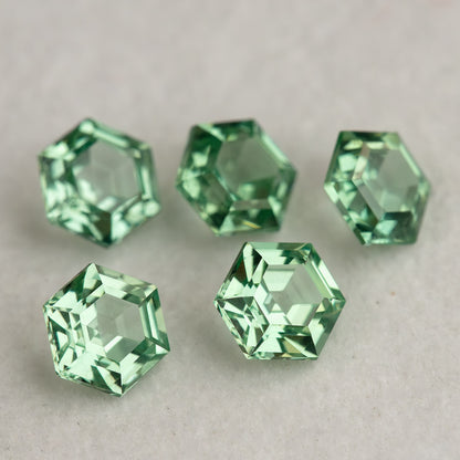Five mint green hexagonal lab-grown sapphires on a neutral base, with pale reflections in their central faces.