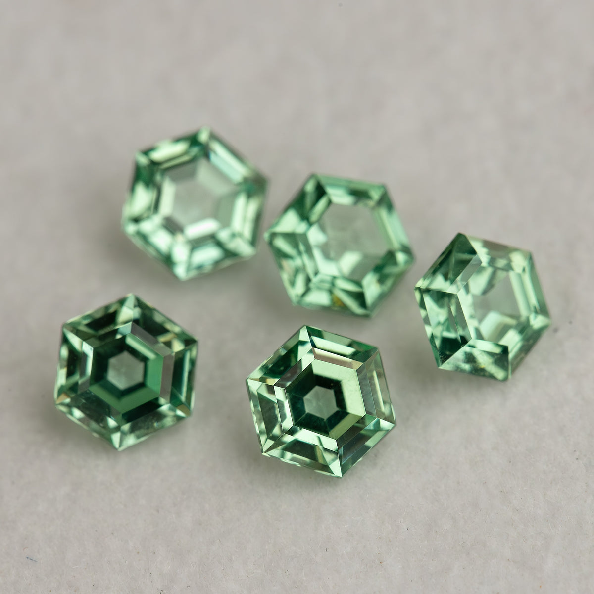 Close group of mint green hexagonal lab-grown sapphires on a grey surface, showing bright edges and green reflections.