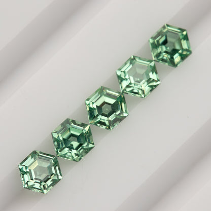 Five mint green hexagonal lab-grown sapphires in a diagonal row on a white grooved tray.