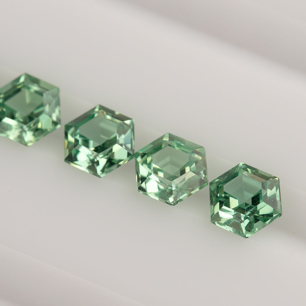 A diagonal row of mint green hexagonal lab-grown sapphires on a white tray, viewed at an angle.
