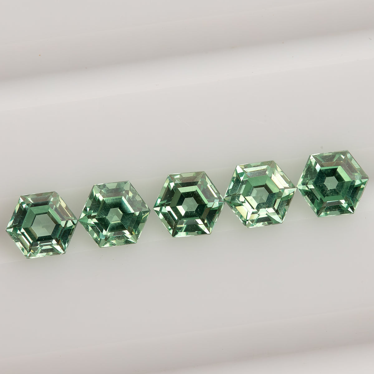 Mint green hexagonal lab-grown sapphires aligned across a white tray, showing their six-sided outlines.