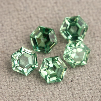 Mint green hexagonal lab-grown sapphires grouped on textured pale grey fabric, with contrasting bright and dark reflections.