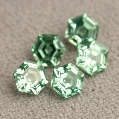 Close-up of a group of mint green hexagonal lab-grown sapphires on textured grey fabric.