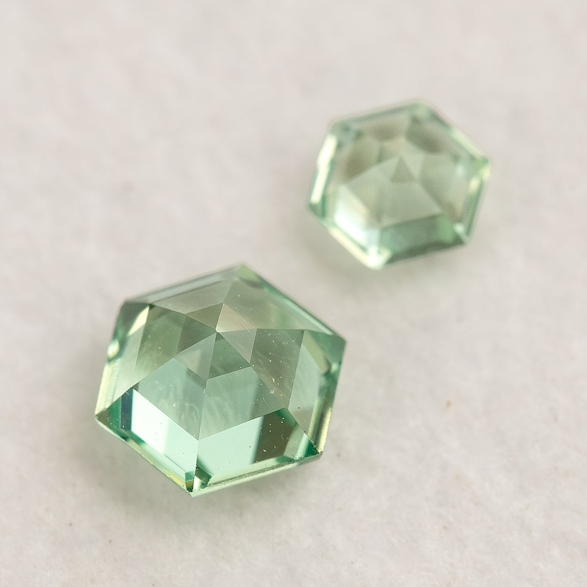 Two mint green hexagonal lab-grown sapphires on a white base, showing their opposite-side facets.