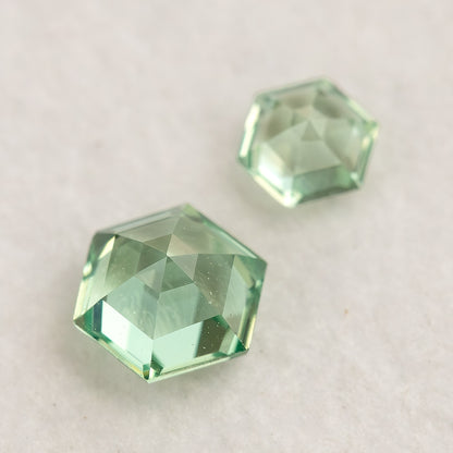 Two mint green hexagonal lab-grown sapphires on a white base, showing their opposite-side facets.