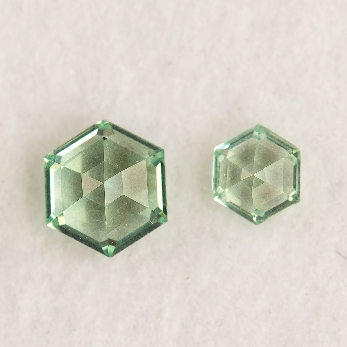 Two differently sized mint green hexagonal lab-grown sapphires with converging opposite-side facets visible on white.