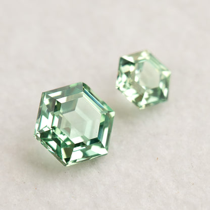 Two mint green hexagonal lab-grown sapphires on a white surface, viewed at a tilt with pale reflections.