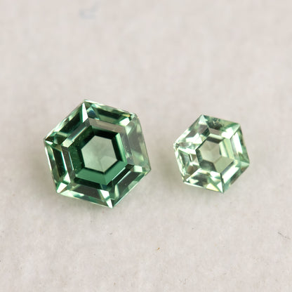 Larger and smaller mint green hexagonal lab-grown sapphires face-up on a white surface, showing flat tables and contrasting green reflections.