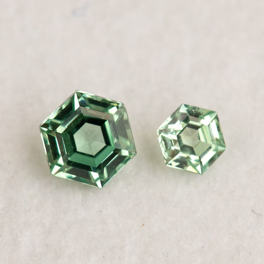 Larger and smaller mint green hexagonal lab-grown sapphires face-up on a white surface, showing flat tables and contrasting green reflections.