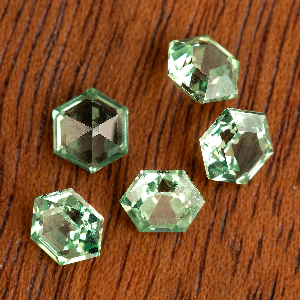 Mint green hexagonal lab-grown sapphires spread across a wood-grain surface, showing varied reflections.