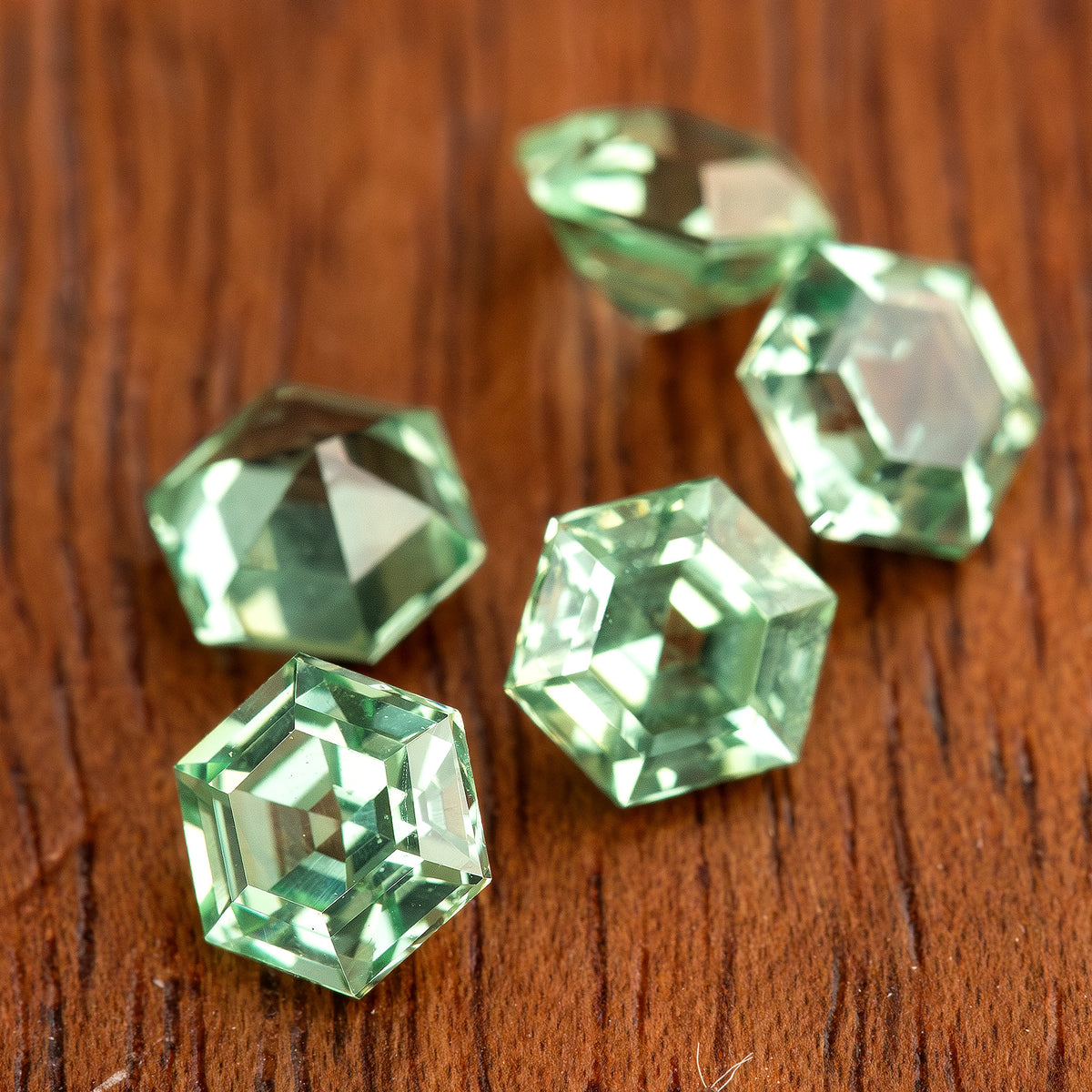 Mint green hexagonal lab-grown sapphires at varied angles on wood, with bright reflective facets.