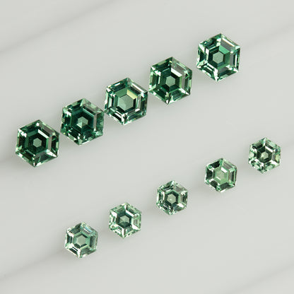 Larger and smaller mint green hexagonal lab-grown sapphires arranged in two diagonal rows on a white tray.