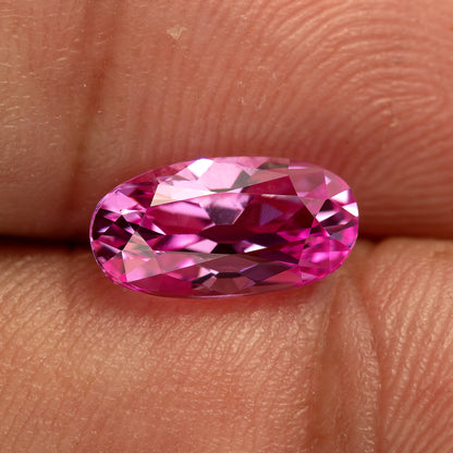 Horizontal fingertip view of the pink moval sapphire with broad pale reflections and dark facets across its face.
