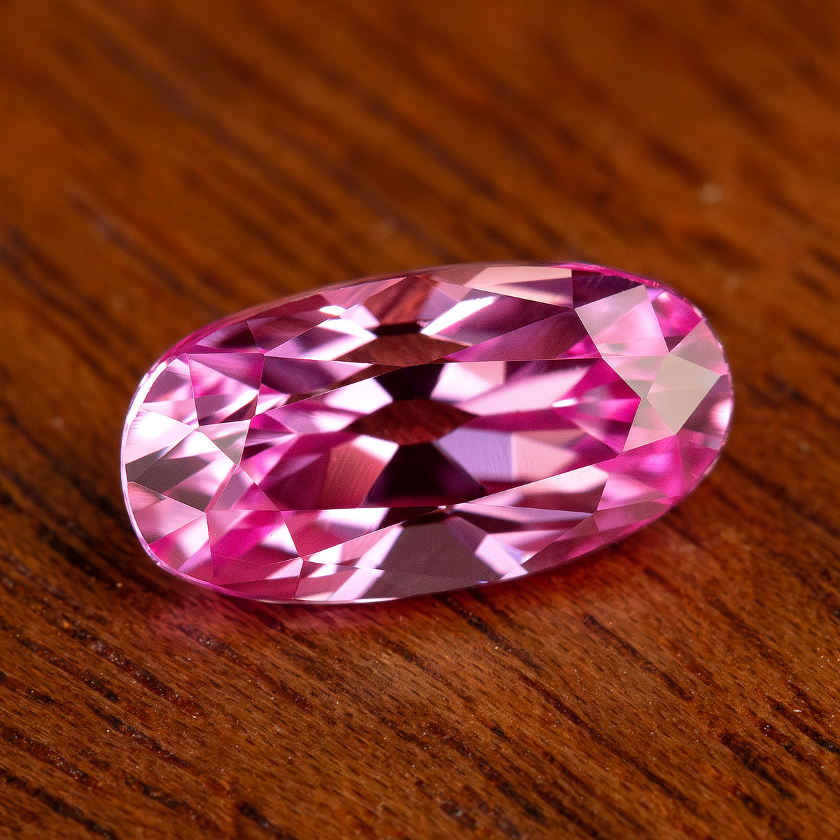 Pink moval sapphire tilted on a wooden surface, with broad white flashes and deep fuchsia reflected areas.