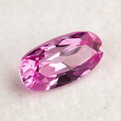 Oblique low-angle view of the pink moval sapphire on a pale surface, showing broad reflective facets and the raised edge of the stone.