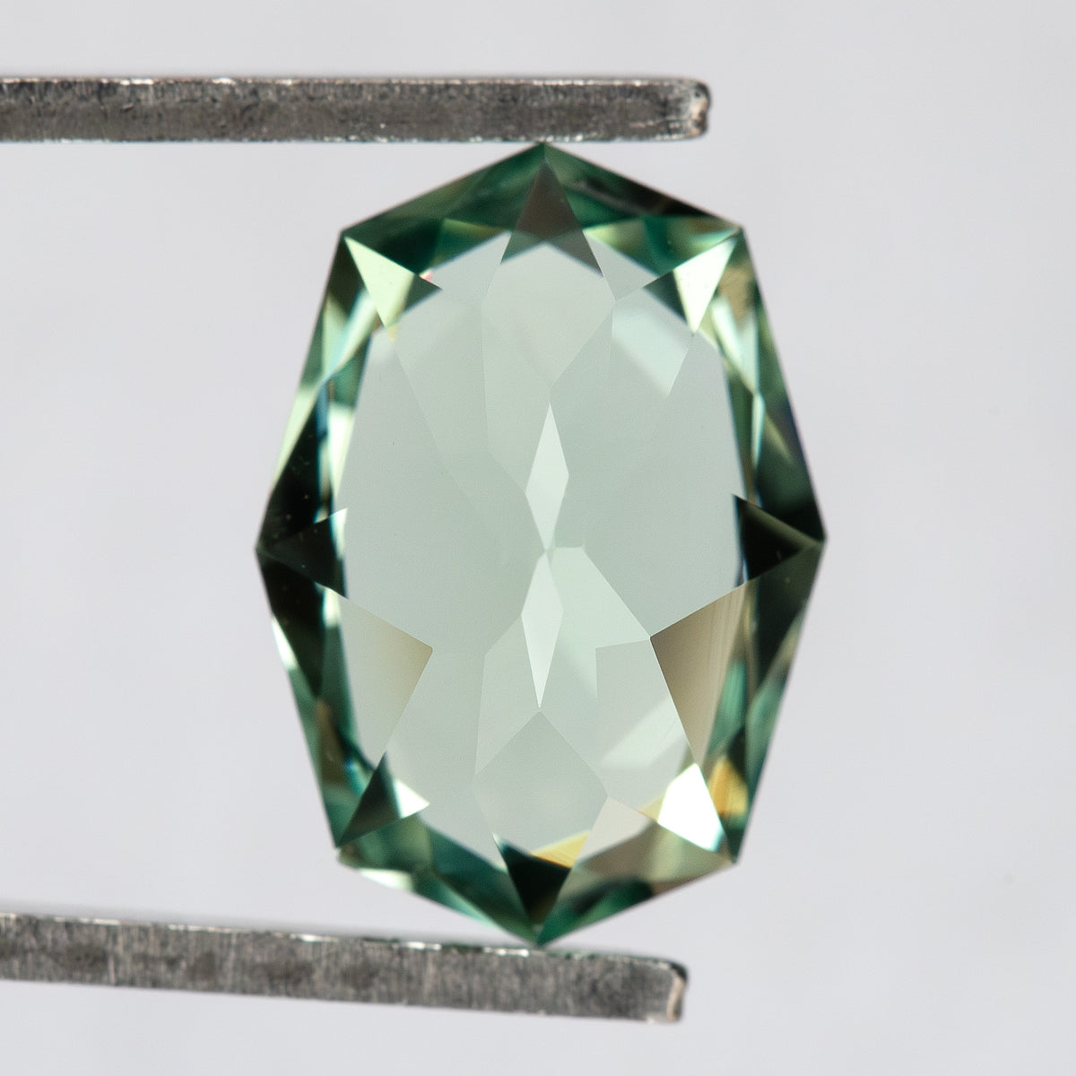 Pavilion and back view of the BLS111 mint green lab-grown sapphire in tweezers.