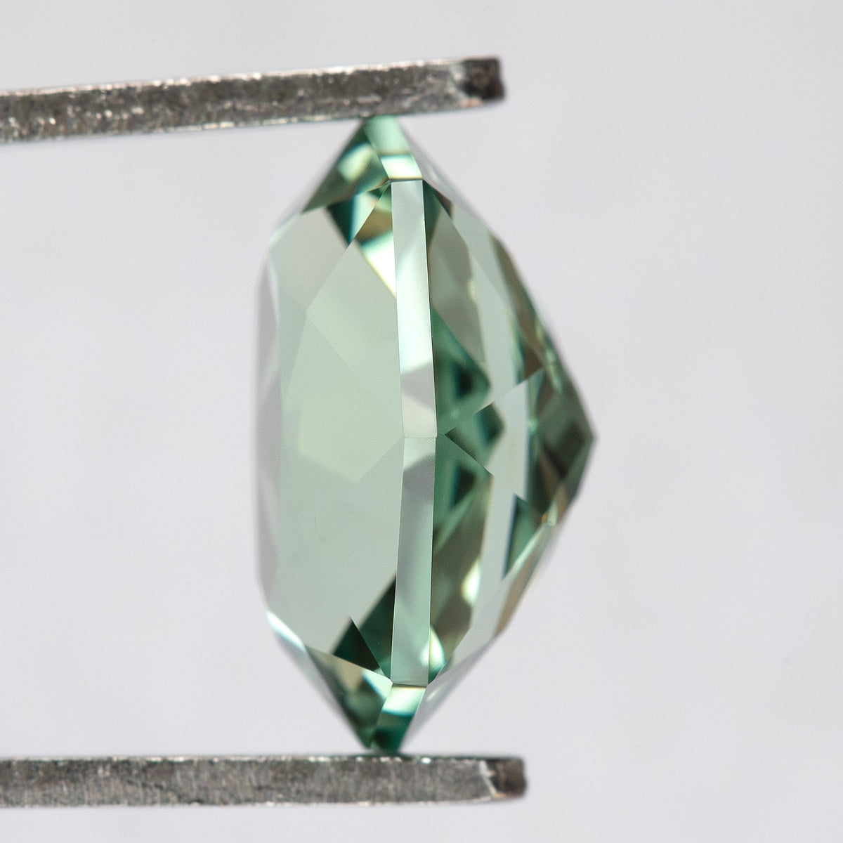 Side profile of BLS111 in tweezers, showing the depth and faceted girdle of the lab-grown sapphire.