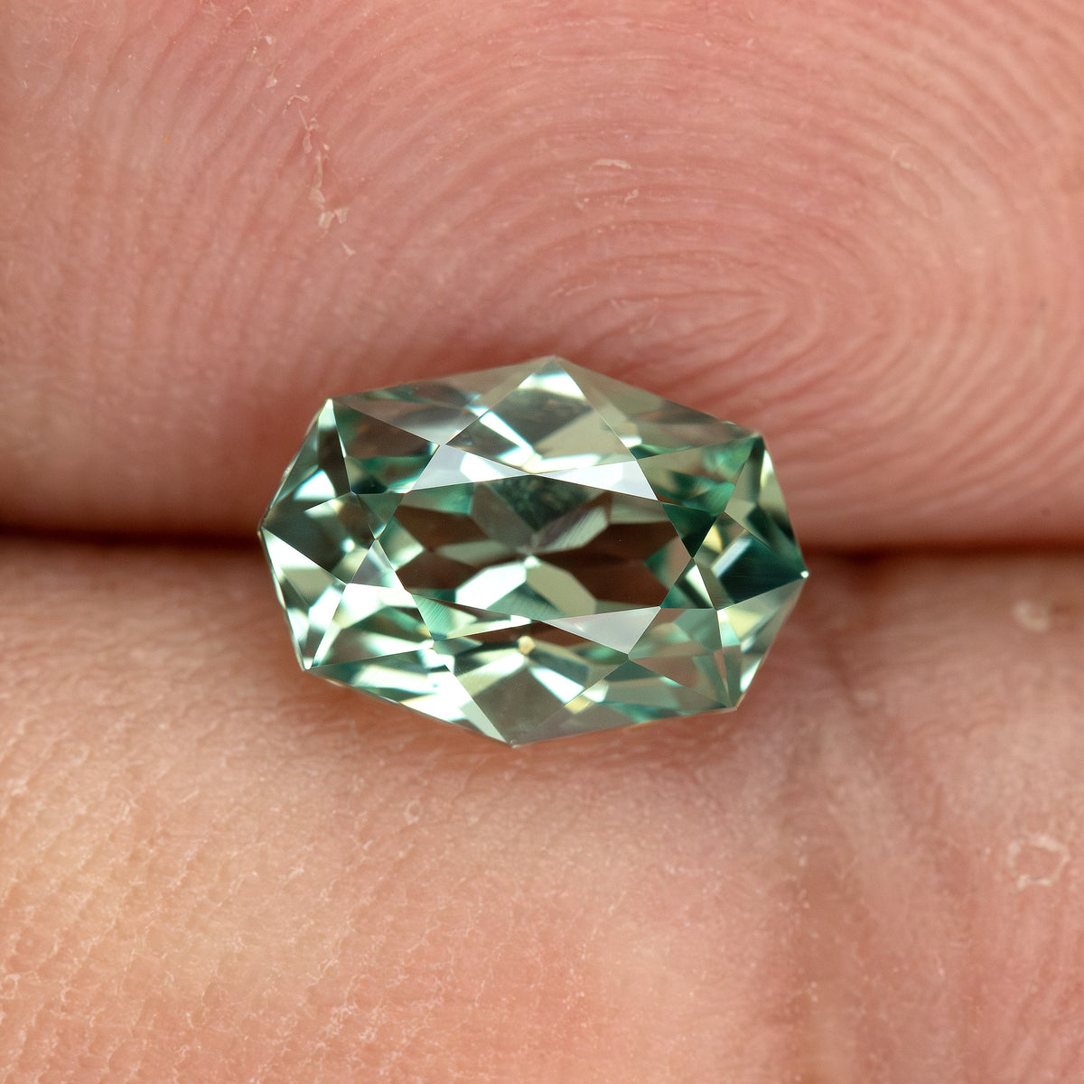 BLS111 mint green lab-grown sapphire on a fingertip for an approximate sense of its 8.5 x 6 mm face-up size.