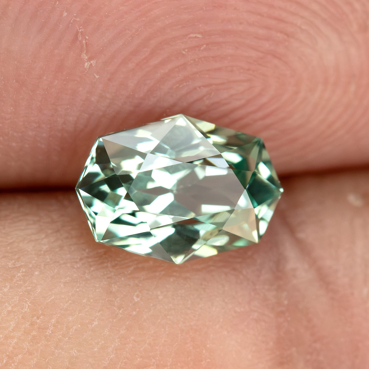 Alternate fingertip view of BLS111 mint green lab-grown sapphire, showing its facet reflections.