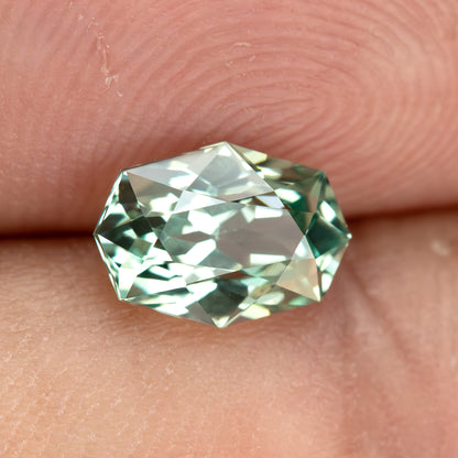 Alternate fingertip view of BLS111 mint green lab-grown sapphire, showing its facet reflections.
